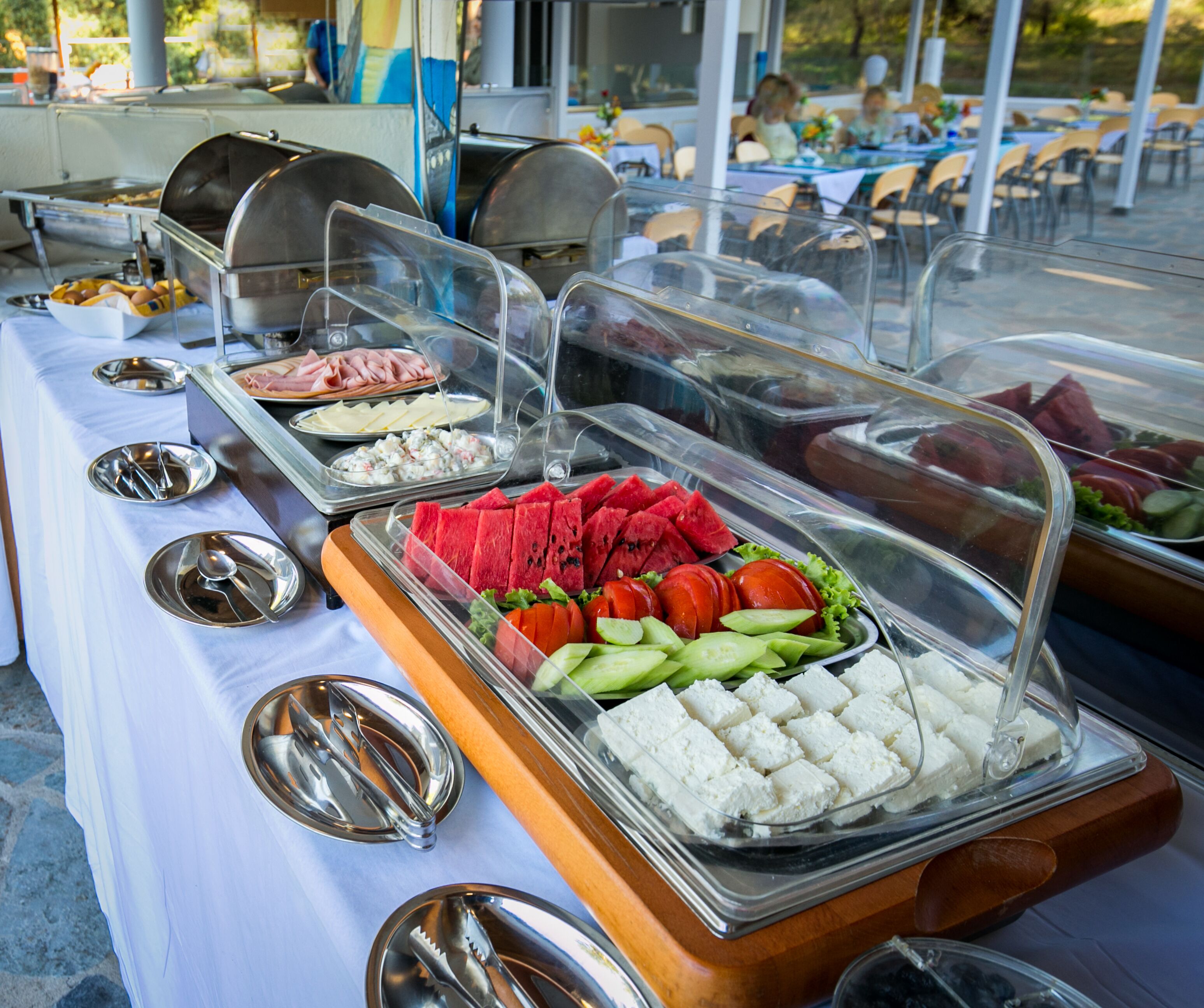 Een buffettafel met verschillende soorten eten, zoals vlees, fruit en groenten, afgedekt met transparante plastic koepels.