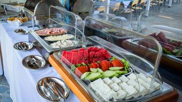 Een buffettafel met verschillende soorten eten, zoals vlees, fruit en groenten, afgedekt met transparante plastic koepels.