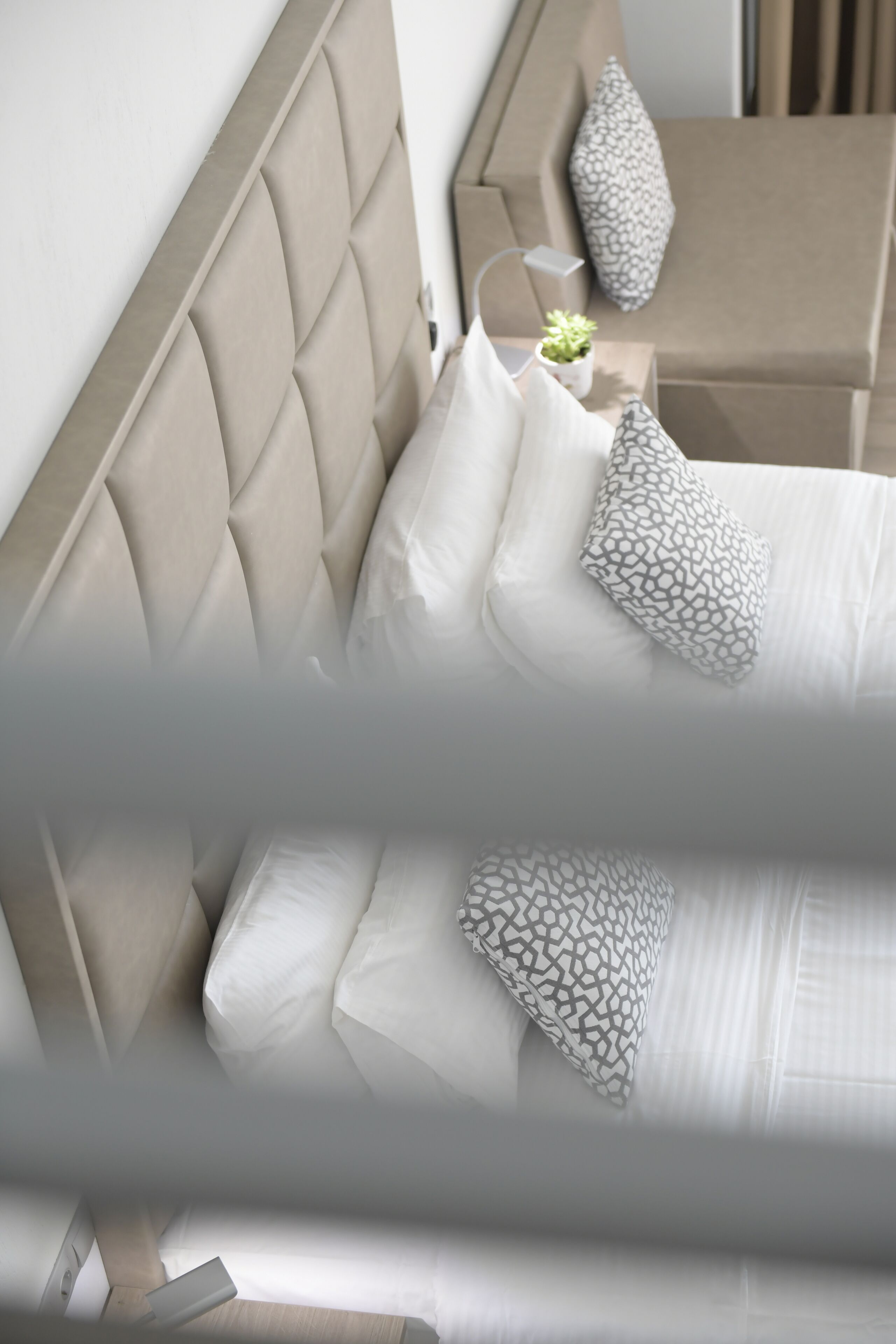 Een bed met een gestoffeerd hoofdbord, witte beddengoed en gestreepte kussens.