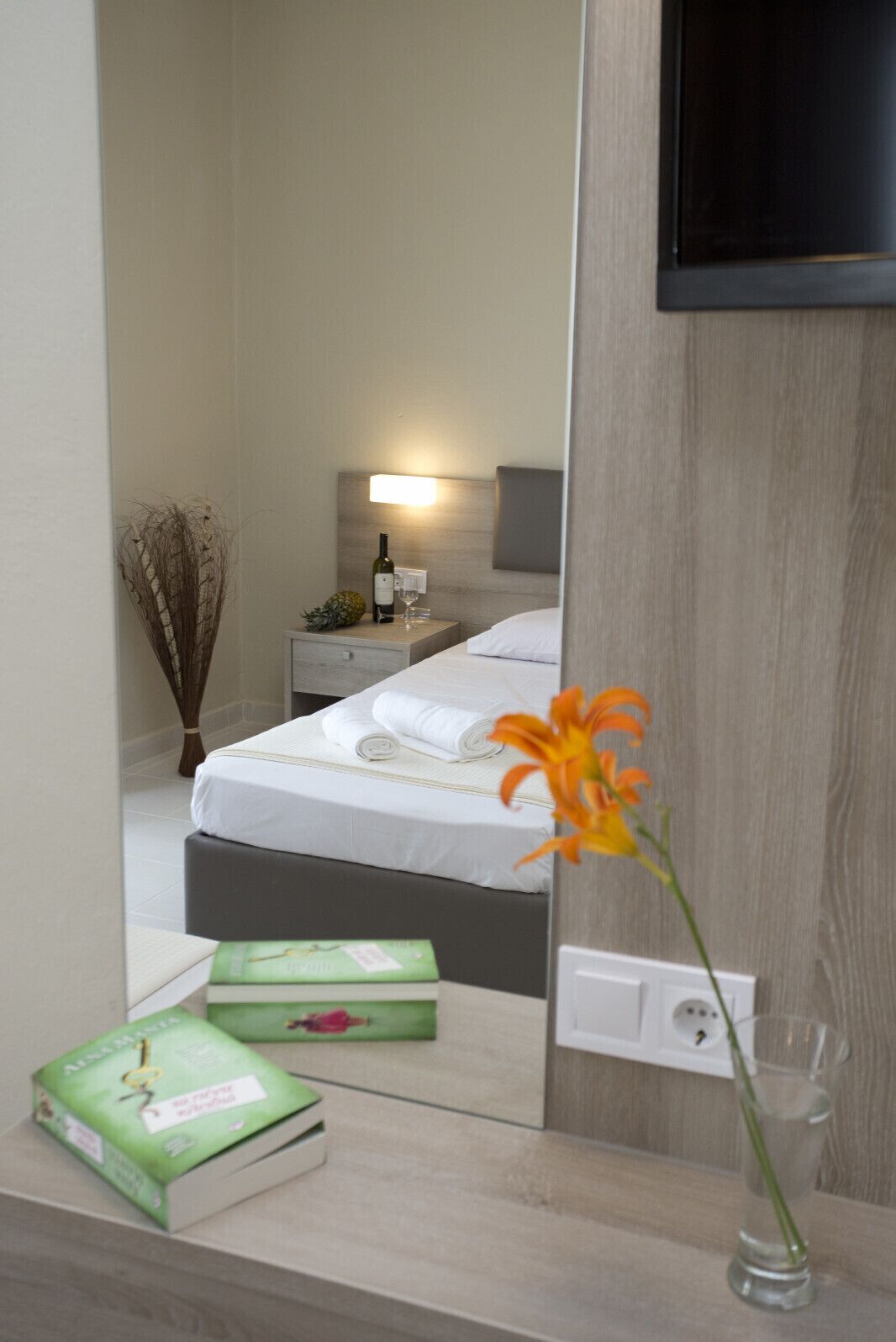 Une chambre d’hôtel avec un lit, une table de chevet, une lampe et un miroir qui reflète la pièce.