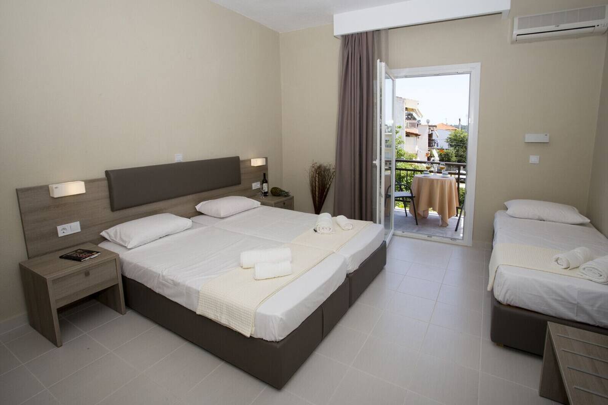 Une chambre d’hôtel avec un grand lit, un lit plus petit, une table de chevet, une table avec une chaise et un balcon avec une table et des chaises.