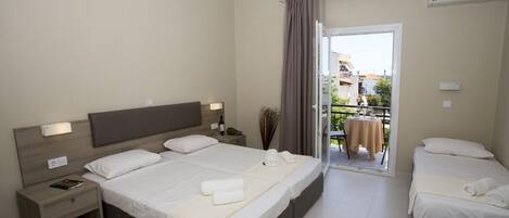 A hotel room with a large bed, a smaller bed, a nightstand, a table with a chair, and a balcony with a table and chairs.