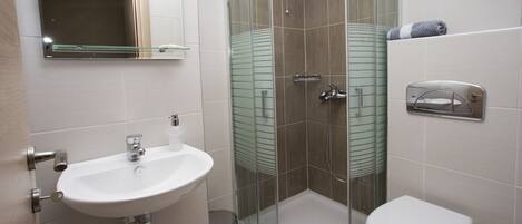 A modern bathroom with a glass-enclosed shower, a white sink, and a toilet.