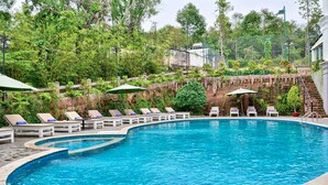 A swimming pool with lounge chairs and umbrellas, surrounded by greenery and a stone wall. - Boulevard Hotel (Phu Quoc)