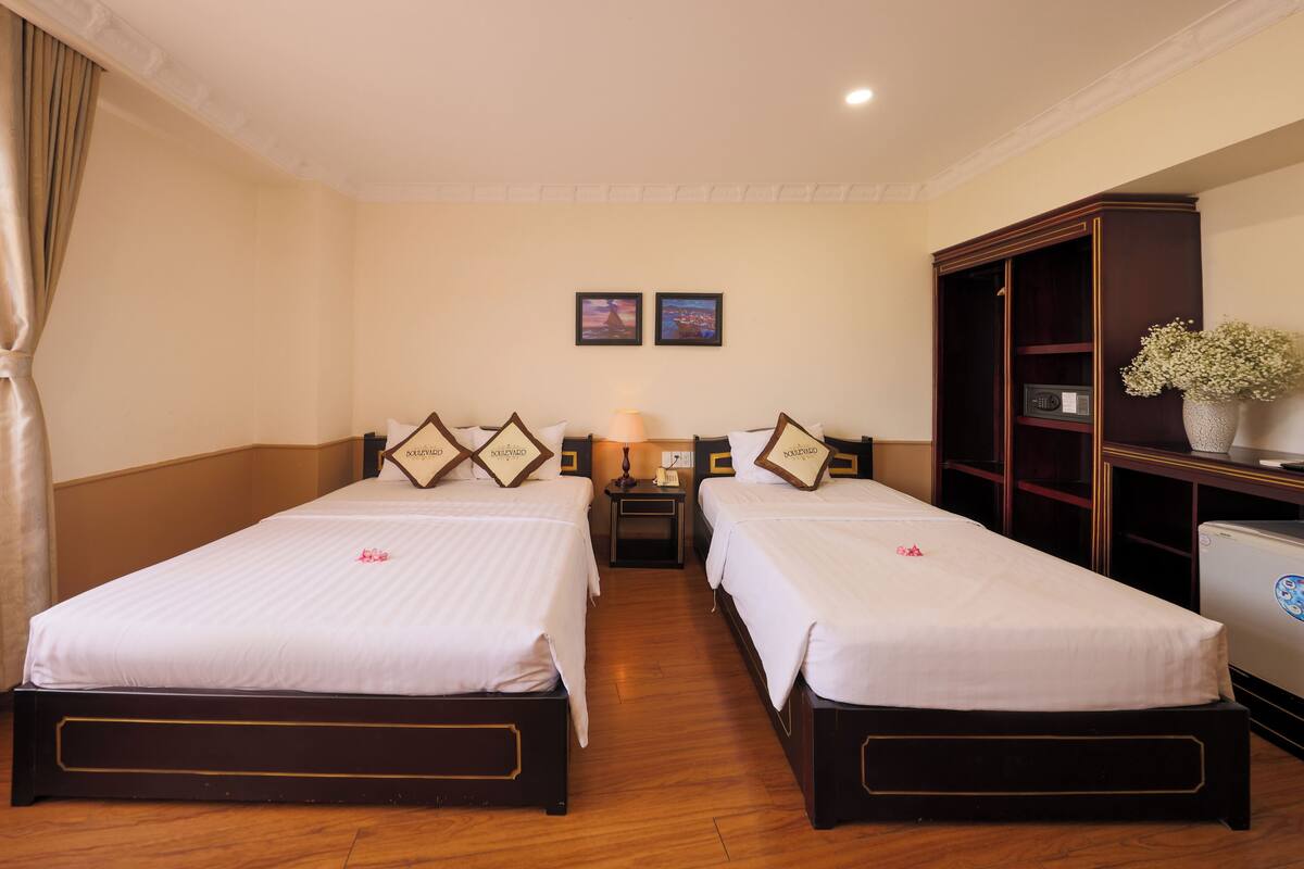 A hotel room with two single beds, a nightstand, a lamp, a dresser, and a small refrigerator.