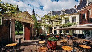 An outdoor café area with brick flooring, wooden tables and chairs, and a covered seating area. - Hotel Prinsenhof (Groningen)