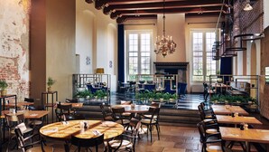 A spacious dining area with high ceilings, exposed brick walls, and large windows allowing natural light. Tables are arranged around a central seating area with a fireplace. - Hotel Prinsenhof (Groningen)