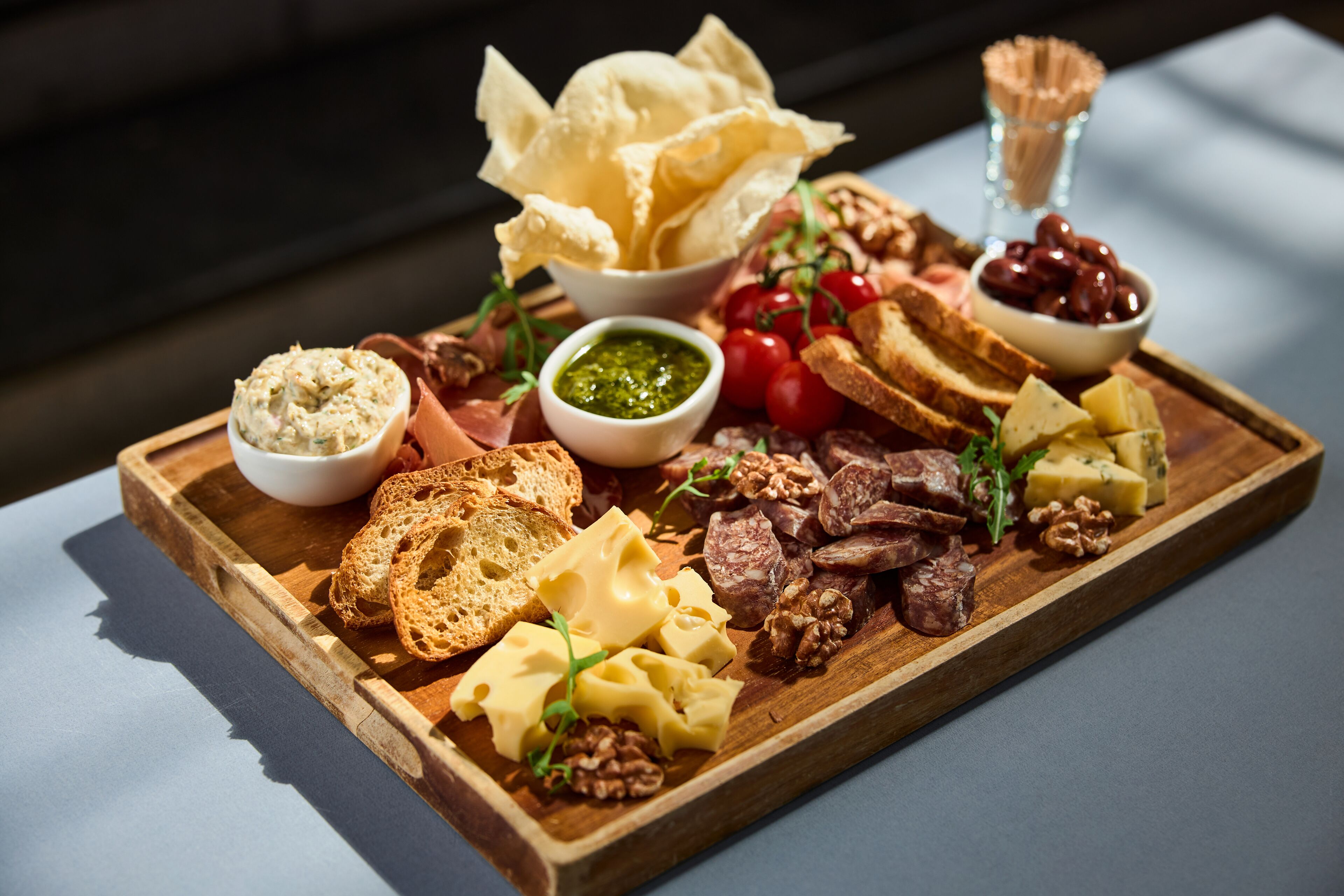 A wooden board with various cheeses, nuts, bread, and olives.
