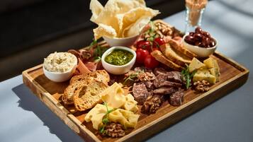 A wooden board with various cheeses, nuts, bread, and olives.