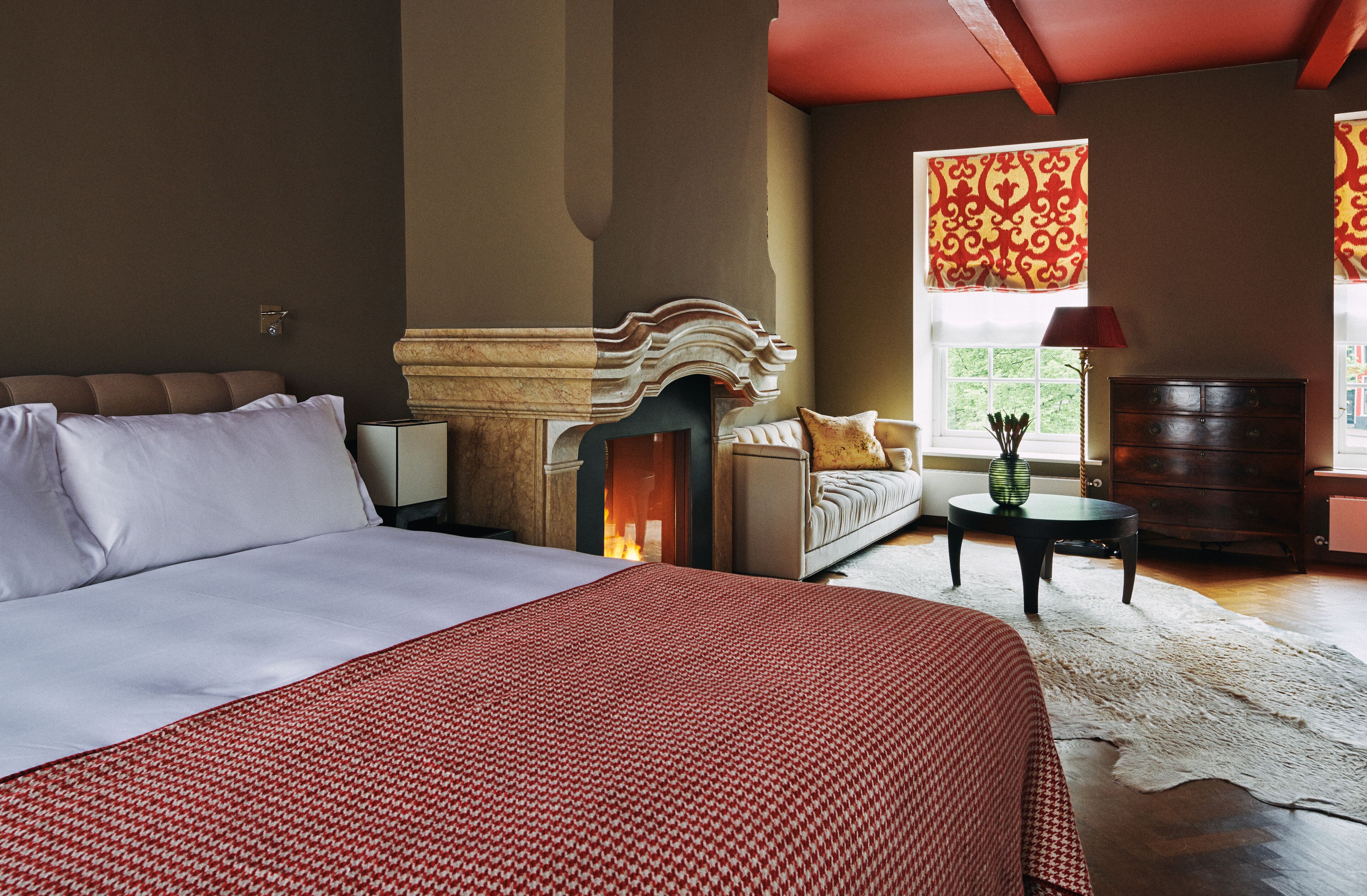 A bedroom with a large bed, a fireplace, a sofa, and a nightstand.