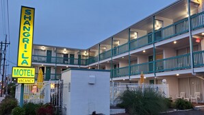 A motel with a sign indicating 'Shangri-La Motel' and 'Vacancy'. It features a multi-story building with balconies and a staircase. - The Shangri La Motel (Ocean City)