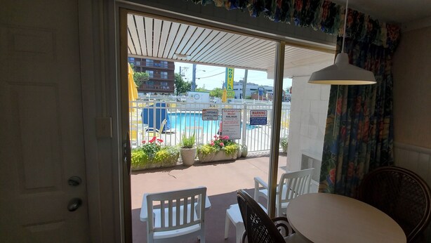 A room with a view of a pool area, a white chair, a table, and a hanging lamp. - The Shangri La Motel (Ocean City)
