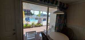 A room with a view of a pool area, a white chair, a table, and a hanging lamp. - The Shangri La Motel (Ocean City)
