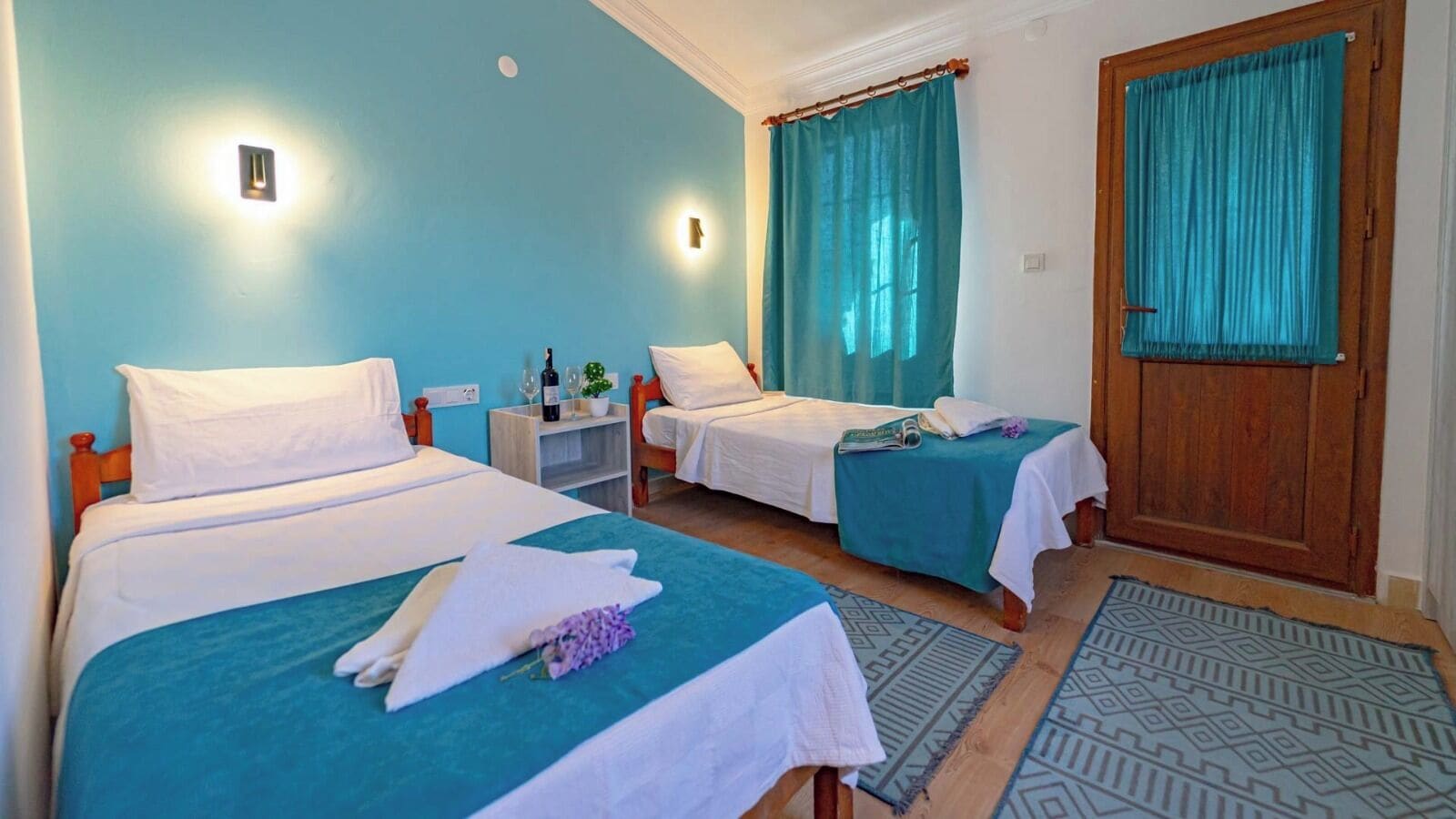 Une chambre d’hôtel avec deux lits, une porte en bois et une fenêtre avec des rideaux.
