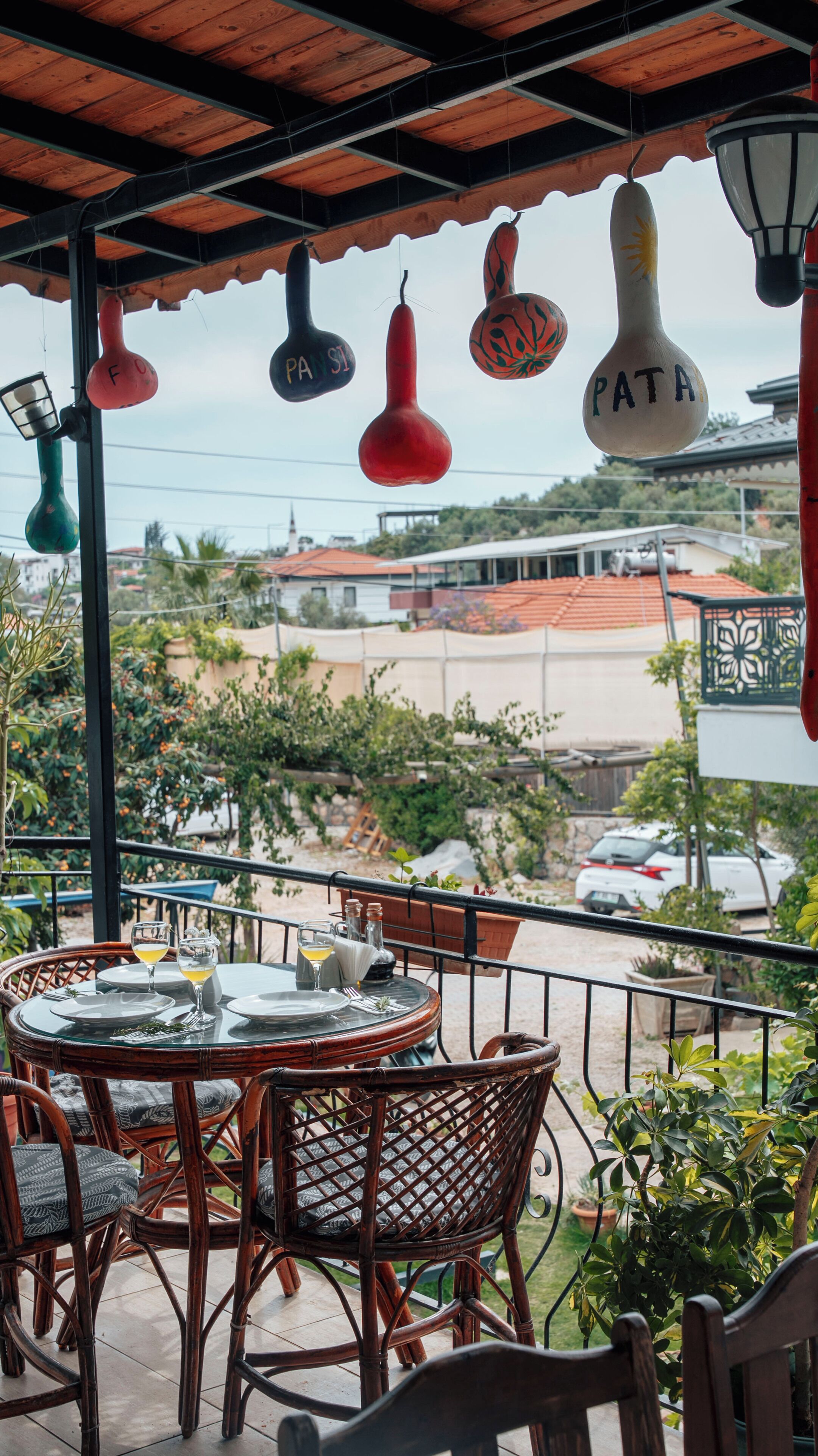 Un balcon agrémenté de meubles en osier, une table dressée pour deux personnes et des objets décoratifs suspendus.