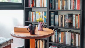Una biblioteca con estanterías, una mesa de madera con un jarrón de flores y una silla.