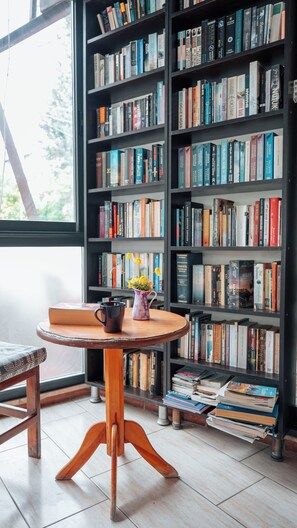 A library with bookshelves, a wooden table with a vase of flowers, and a chair. - Flower Pension Hotel (Kas)