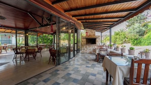 Un patio al aire libre con mesas y sillas, una chimenea de piedra y vistas a vegetación.