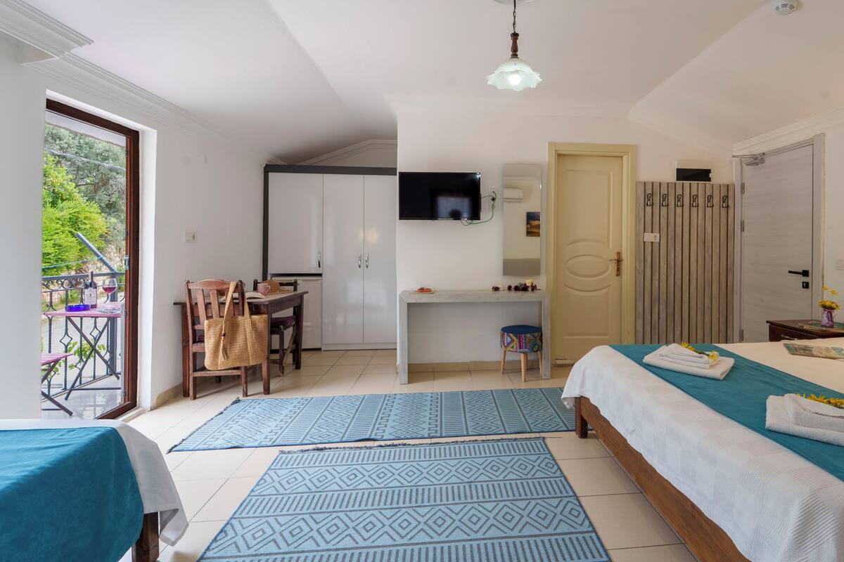 A hotel room with a bed, a desk, a chair, a small table with a chair, a wardrobe, and a television.