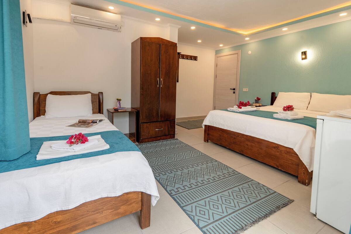 A hotel room with two beds, a wardrobe, a small table, and a wall-mounted air conditioner.
