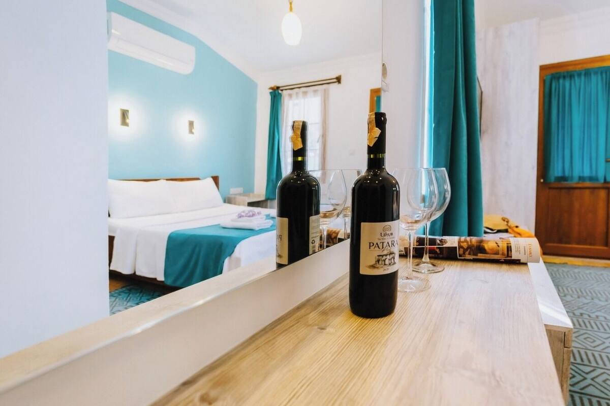 A hotel room with a wooden table, two bottles of wine, and a glass.