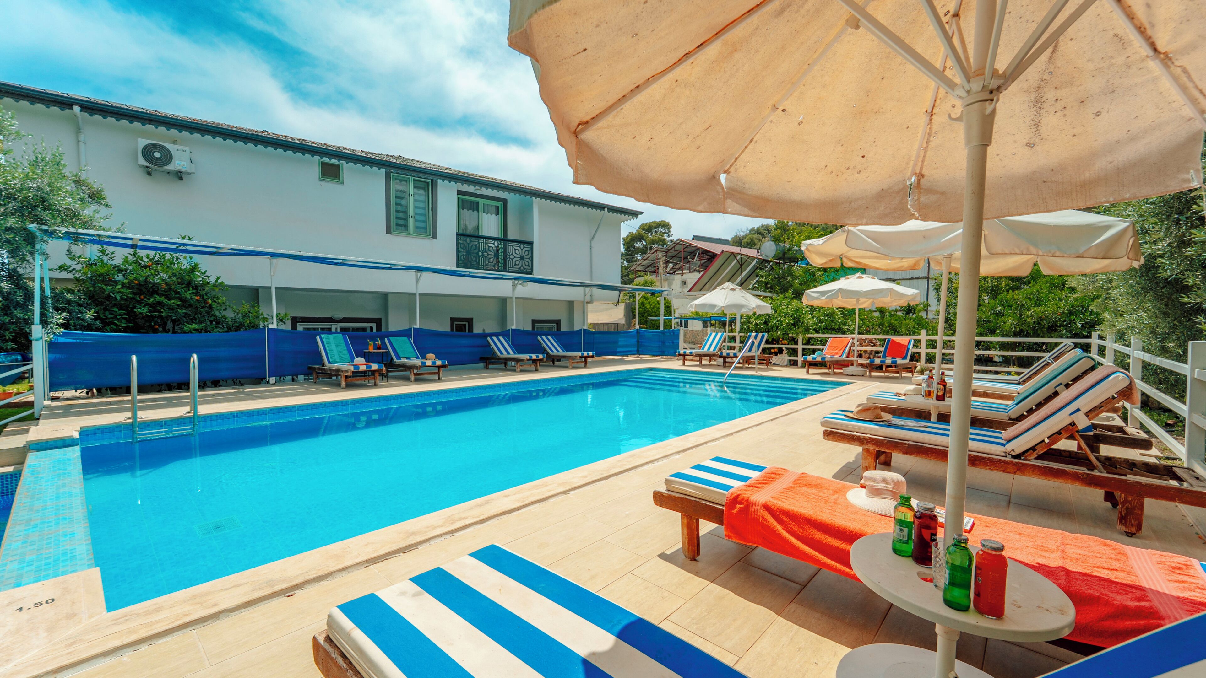 A swimming pool with lounge chairs and umbrellas, surrounded by a building with a white facade and a covered area.