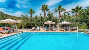 A swimming pool with lounge chairs and umbrellas, surrounded by palm trees and greenery.