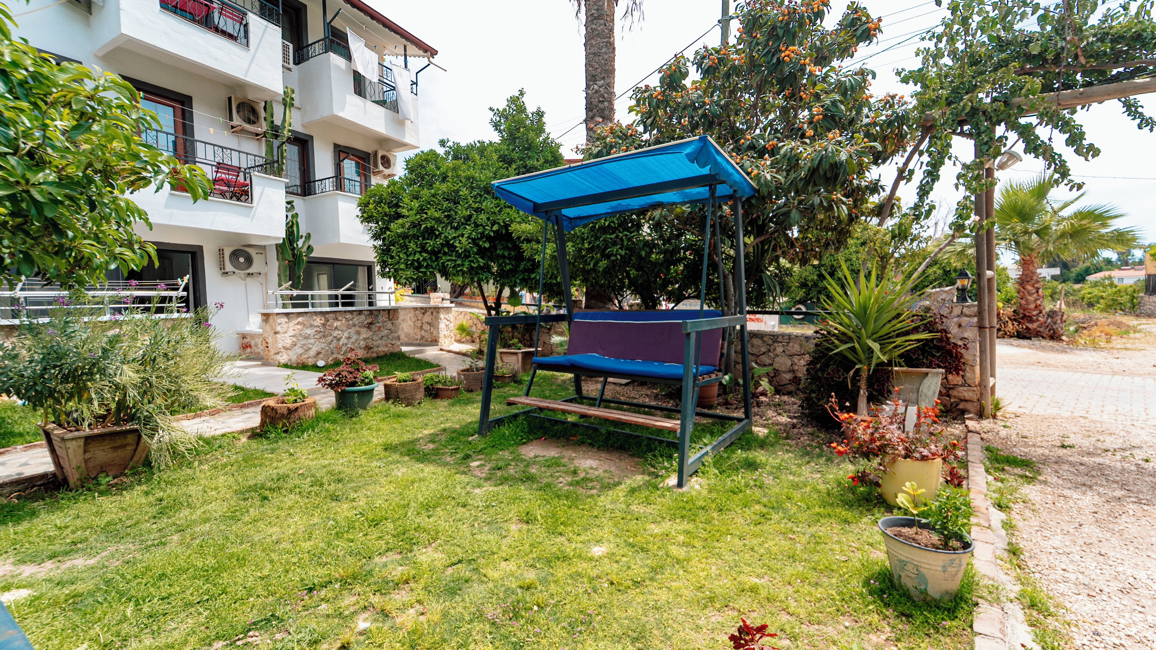 A garden area with a swing set, potted plants, and a building with balconies.