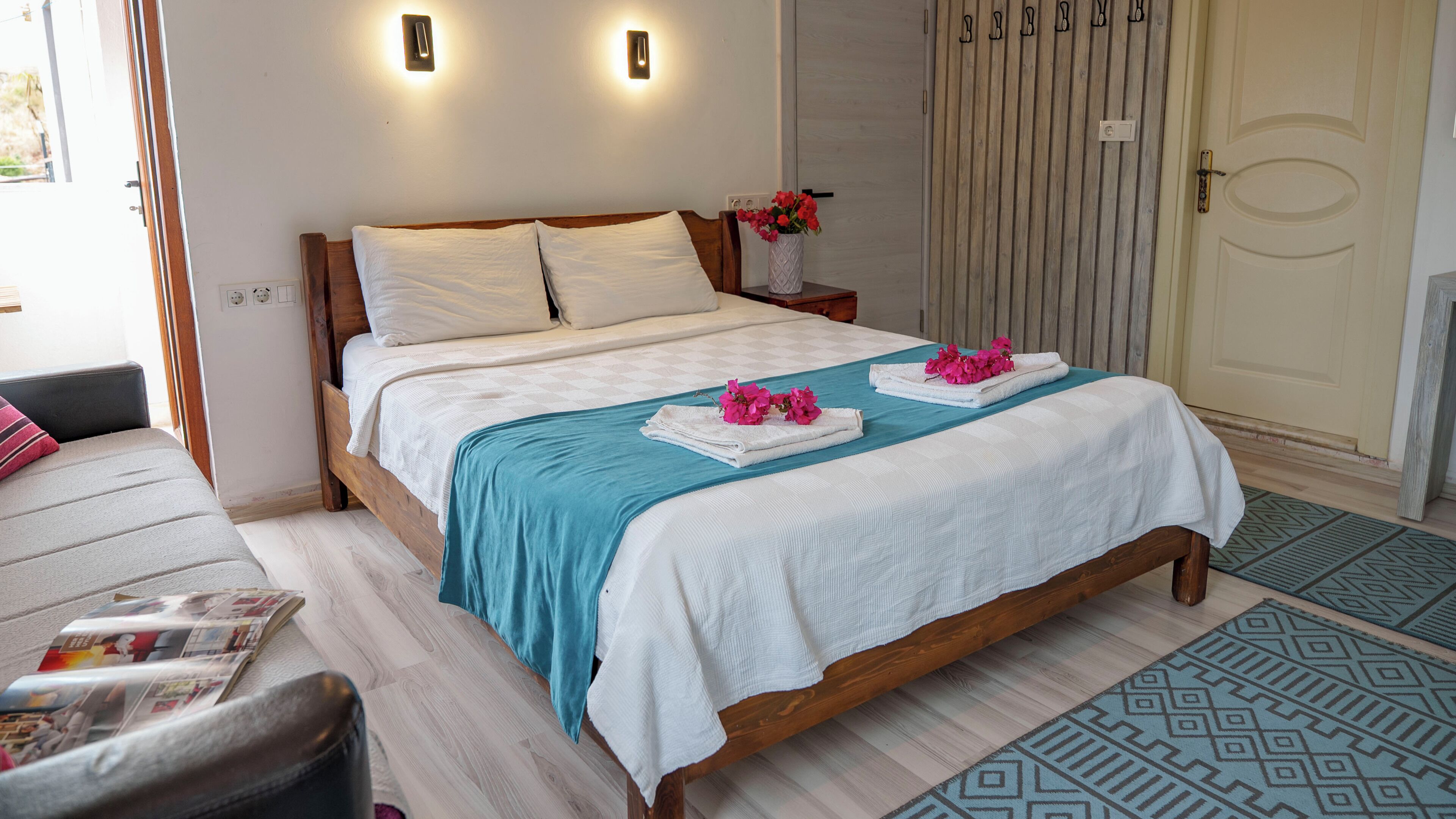 Una cama bien tendida con una colcha azul, almohadas blancas y flores rosas sobre una toalla blanca.