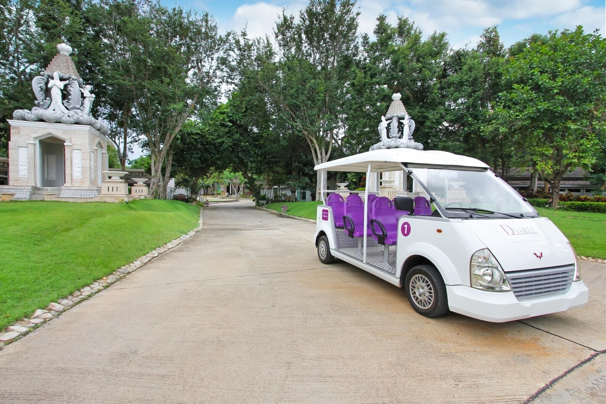 A white and purple golf cart parked on a paved path with a statue and greenery in the background.