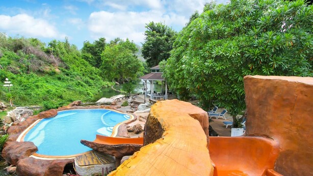 A natural pool surrounded by rocks and trees, with a wooden slide leading into it.