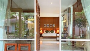 A modern bedroom with a large bed, bedside tables, and a view of a lush garden through large windows.