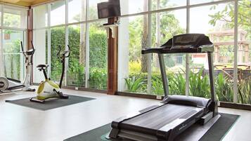 Un gimnasio con equipo de ejercicio, ventanas amplias y vistas al verdor.
