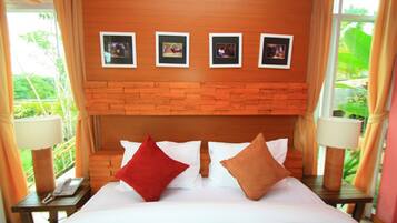 A hotel room with a wooden headboard, a bed with white and red pillows, a nightstand with a lamp, and a window with curtains.