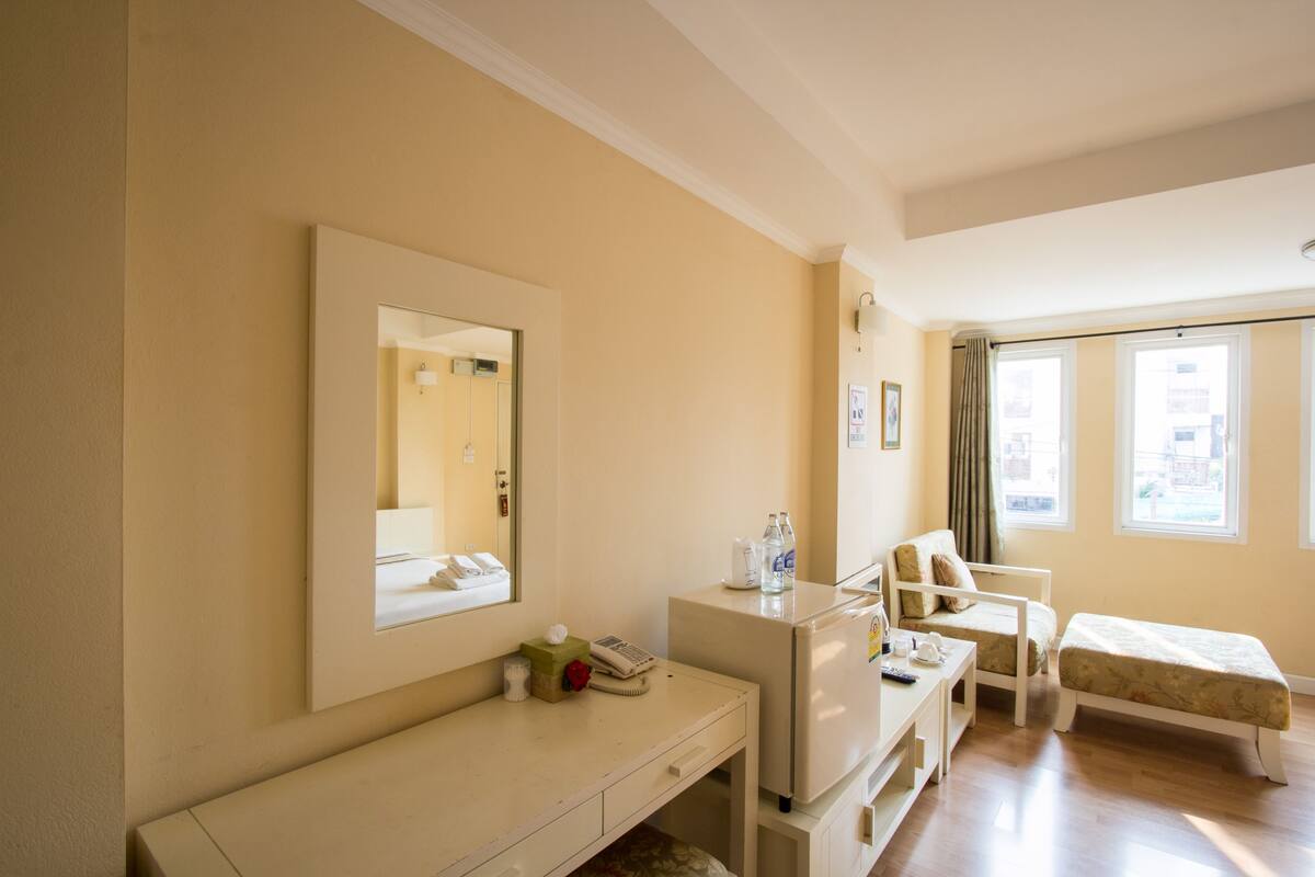 A hotel room with a bed, a desk with a telephone, a mirror, and a window with curtains.