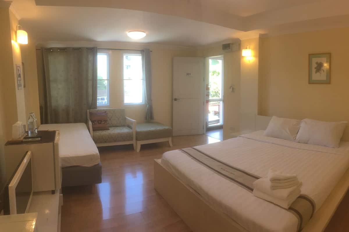 A hotel room with a bed, a desk, a chair, a bathroom with a toilet and shower, and a door to a balcony.