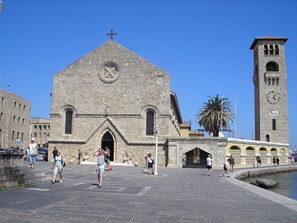 Una iglesia histórica con una torre de campanario, una gran entrada en arco y un área pavimentada circundante.