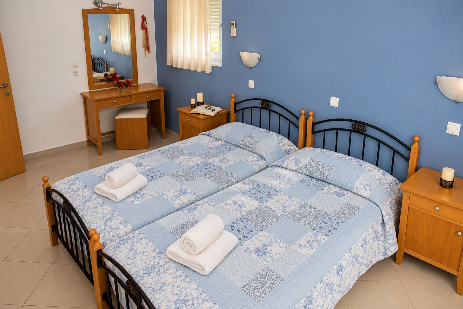 A bedroom with a double bed, a wooden desk, a chair, a nightstand, and a mirror.