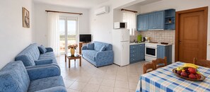A living room with a sofa, a television, and a dining area with a table set for two. - Nephele Apartments (Rhodes)