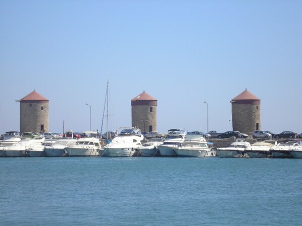 Un puerto deportivo con varias embarcaciones amarradas y tres torres al fondo.