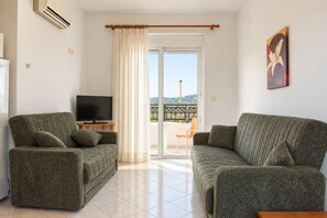A living room with two sofas, a television, and a sliding glass door leading to an outdoor area. - Nephele Apartments (Rhodes)