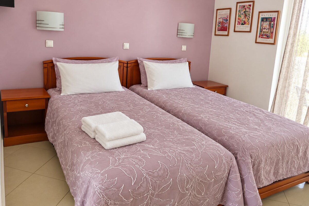 Una cama doble con colcha estampada floral, una mesita de noche con cajón y un aplique de pared.