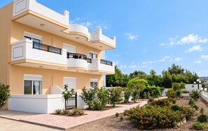A multi-story residential building with balconies, a paved garden area, and a clear sky. - Nephele Apartments (Rhodes)
