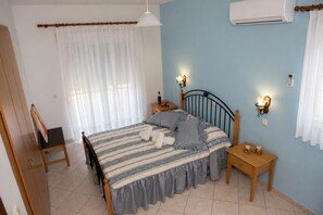 A bedroom with a bed, a nightstand, a wall-mounted lamp, and an air conditioning unit. - Nephele Apartments (Rhodes)