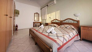 A hotel room with a wooden bed, a nightstand, a bedside table, a mirror, and a fire extinguisher. - Nephele Apartments (Rhodes)