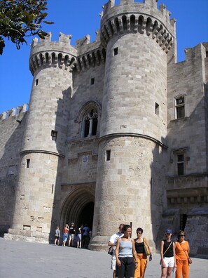 Un castillo histórico con una gran torre central y torres más pequeñas, que presenta ventanales de arco y almenas.