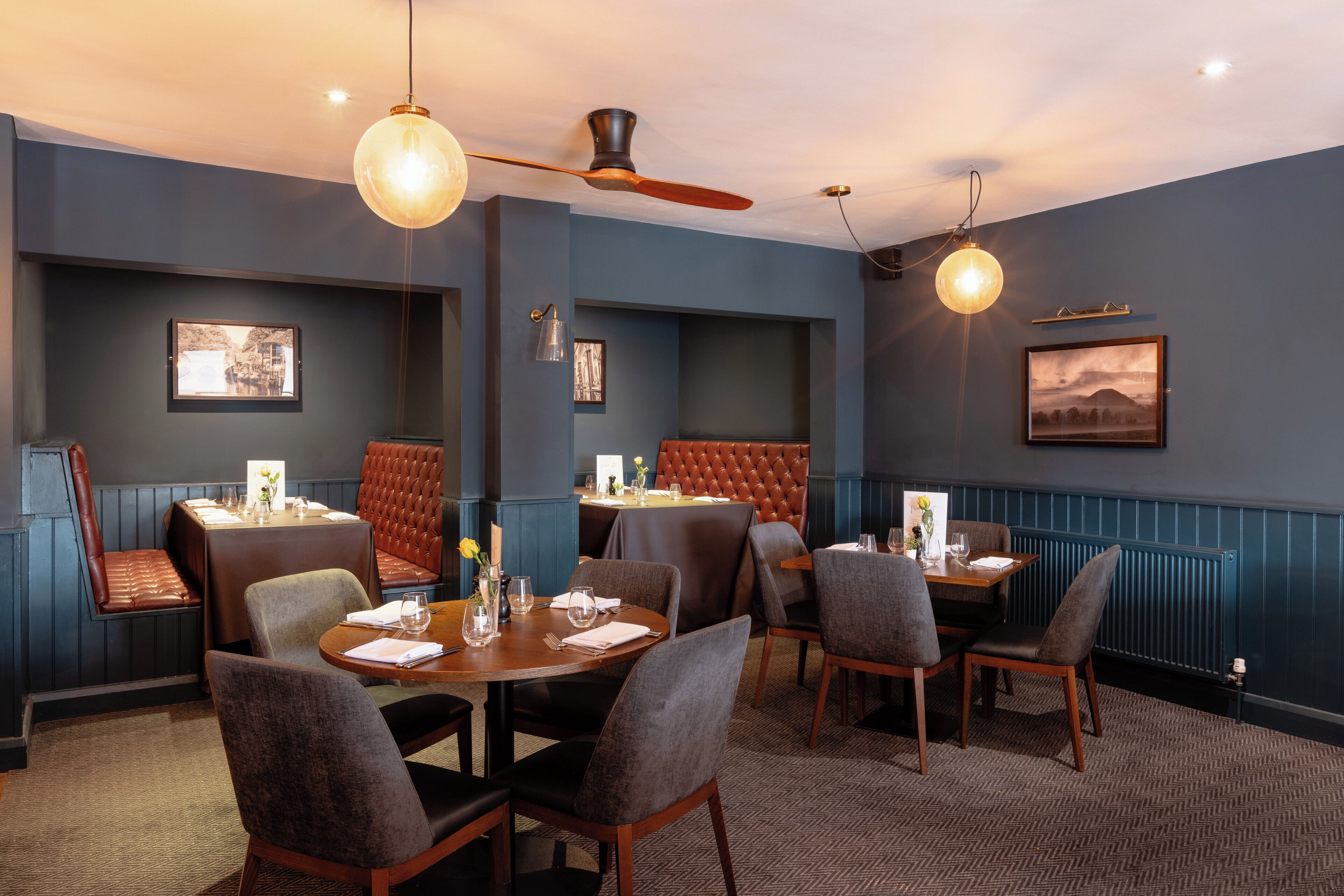 A dining area with multiple tables and chairs, ceiling fans, and wall-mounted lighting fixtures.