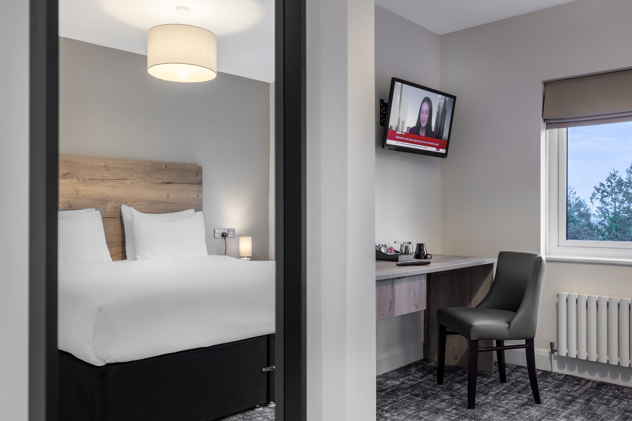A hotel room with a bed, a desk, a chair, a television, and a window.