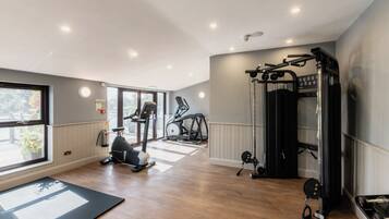 Un gimnasio con equipo de ejercicio, ventanas amplias y pisos de madera.