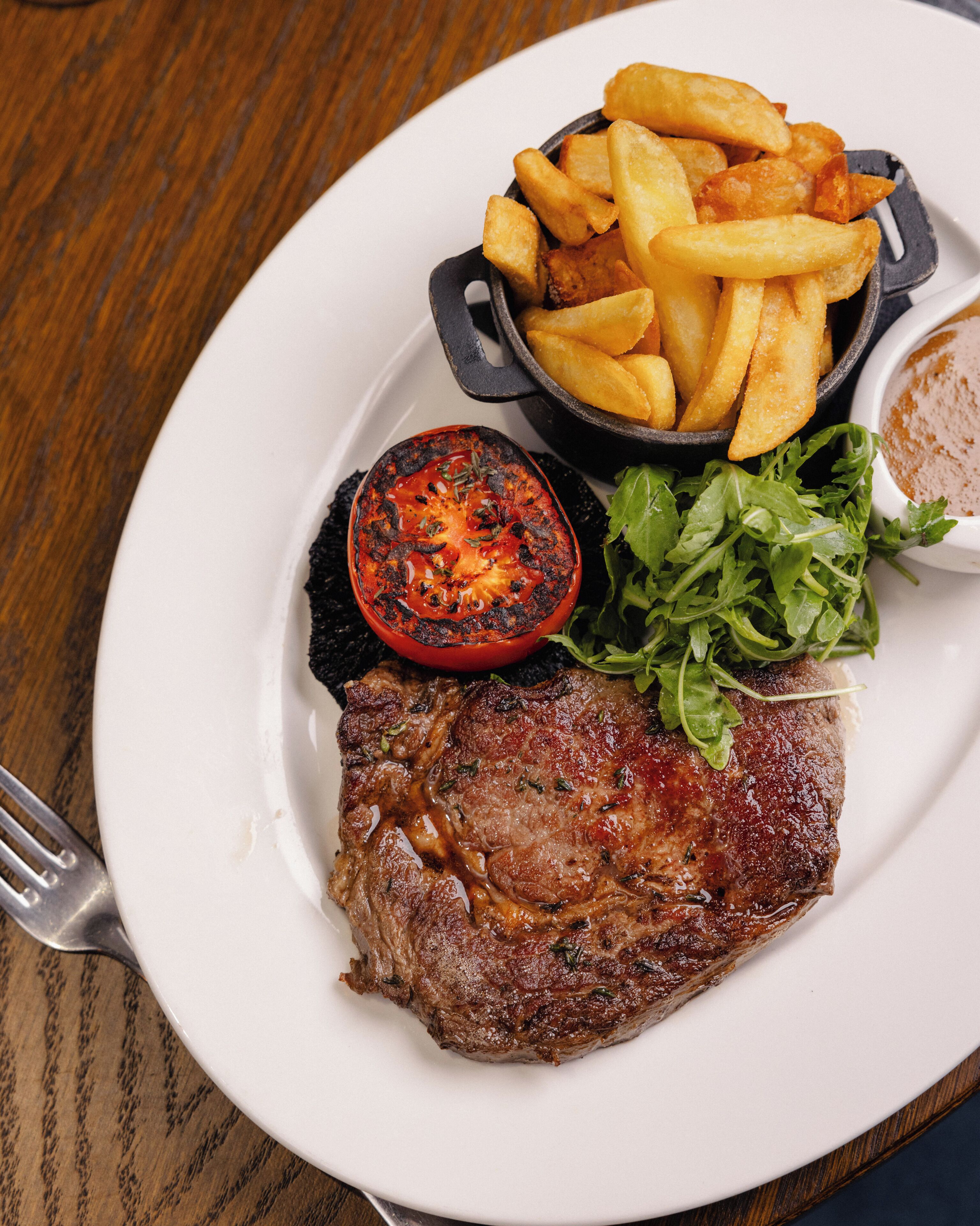 A plate with a steak, fries, and a grilled tomato.